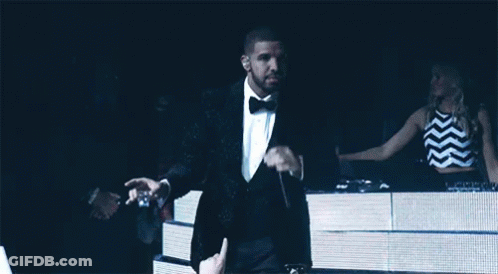 A Man In A Tuxedo Is Holding A Microphone In Front Of A Crowd GIF