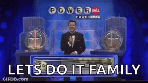 A Man In A Tuxedo Is Holding A Microphone In Front Of A Powerball Lottery Machine . GIF