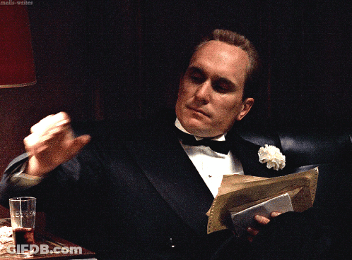 A Man In A Tuxedo Is Holding A Piece Of Paper And A Glass Of Water GIF