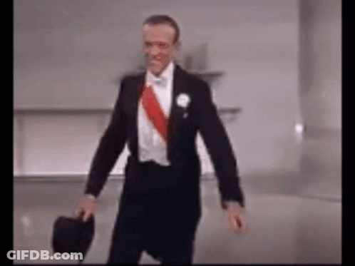 A Man In A Tuxedo Is Holding A Top Hat And Walking . GIF