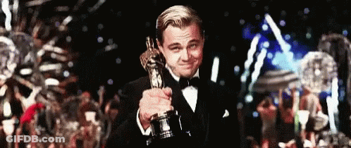 A Man In A Tuxedo Is Holding An Oscar In His Hand . GIF