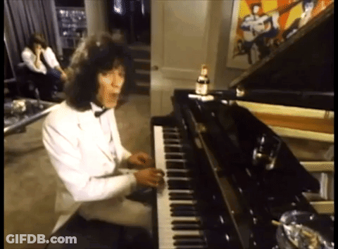 A Man In A Tuxedo Is Playing A Piano In A Room GIF