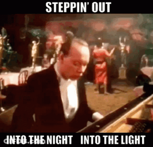 A Man In A Tuxedo Is Playing A Piano In Front Of A Crowd . GIF