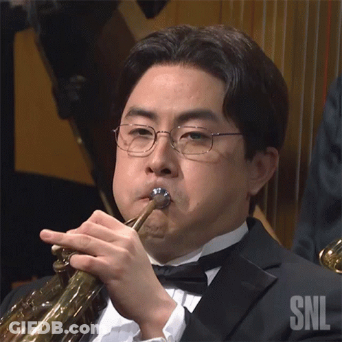 A Man In A Tuxedo Is Playing A Trumpet With A Snl Logo In The Background GIF