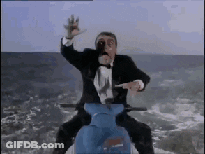 A Man In A Tuxedo Is Riding A Blue Scooter On Top Of A Mountain . GIF