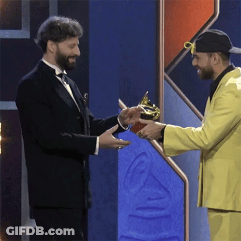 A Man In A Tuxedo Is Shaking Hands With Another Man In A Yellow Suit GIF