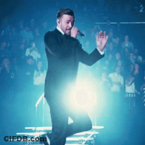 A Man In A Tuxedo Is Singing Into A Microphone In Front Of A Crowd GIF