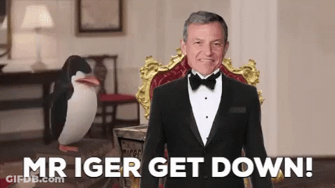 A Man In A Tuxedo Is Sitting In A Chair With The Words Mr Iger Get Down Behind Him GIF