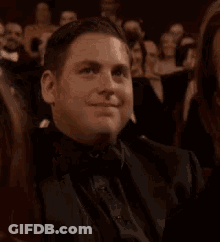 A Man In A Tuxedo Is Sitting In A Crowd Of People And Clapping . GIF