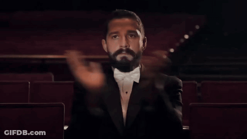 A Man In A Tuxedo Is Sitting In An Auditorium GIF