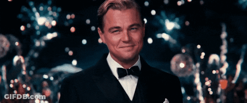 A Man In A Tuxedo Is Smiling In Front Of A Crowd GIF