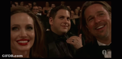 A Man In A Tuxedo Is Smiling In Front Of A Woman With Red Lips GIF