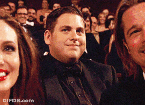 A Man In A Tuxedo Is Smiling While Sitting In A Crowd GIF