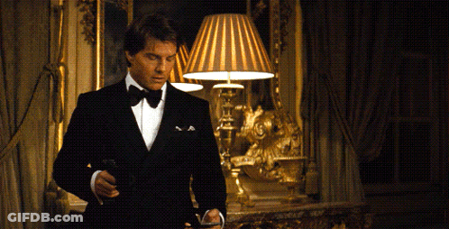 A Man In A Tuxedo Is Standing In A Room With A Lamp GIF