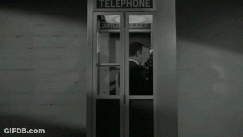 A Man In A Tuxedo Is Standing In A Telephone Booth In A Black And White Photo . GIF
