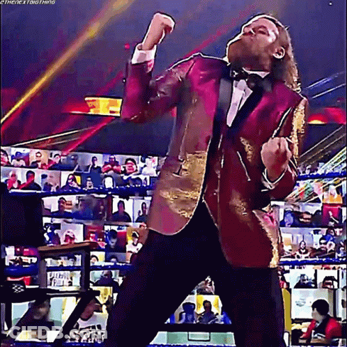 A Man In A Tuxedo Is Standing In A Wrestling Ring With His Arms In The Air . GIF