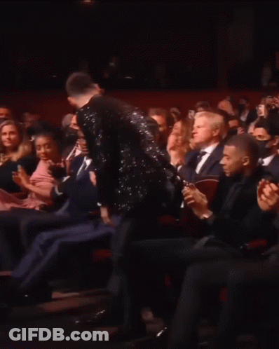 A Man In A Tuxedo Is Standing In Front Of A Crowd Applauding GIF