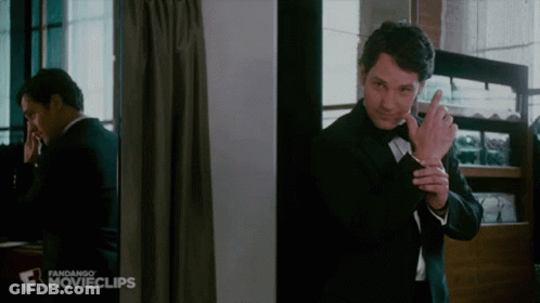 A Man In A Tuxedo Is Standing In Front Of A Mirror And Talking On A Cell Phone . GIF
