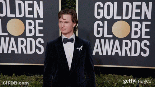 A Man In A Tuxedo Is Standing In Front Of A Sign That Says Golden Globe Awards GIF