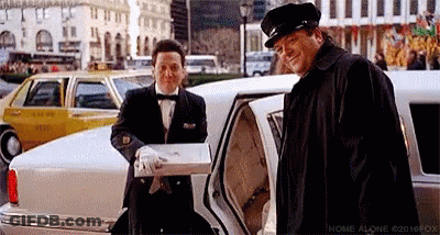 A Man In A Tuxedo Is Standing Next To A Man In A Limousine Holding A Box . GIF