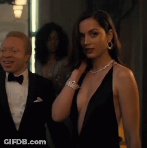 A Man In A Tuxedo Is Standing Next To A Woman In A Plunging Black Dress . GIF