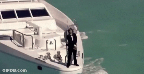 A Man In A Tuxedo Is Standing On The Side Of A Boat In The Ocean . GIF