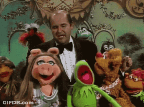 A Man In A Tuxedo Is Surrounded By Muppets Including Kermit GIF