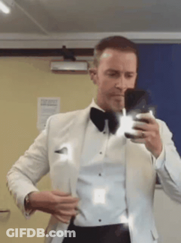 A Man In A Tuxedo Is Taking A Picture Of Himself In A Mirror GIF