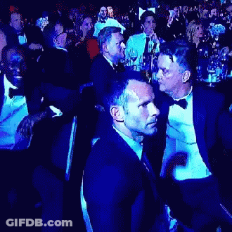 A Man In A Tuxedo Is Talking To Another Man In A Crowd Of People GIF