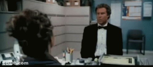 A Man In A Tuxedo Is Talking To Another Man In A Cubicle GIF