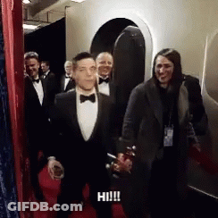 A Man In A Tuxedo Is Walking Down A Red Carpet With A Woman Behind Him . GIF