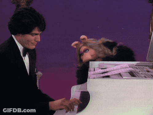 A Man In A Tuxedo Plays A Piano Next To A Stuffed Pig GIF