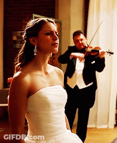 A Man In A Tuxedo Plays A Violin While A Woman In A White Dress Looks On GIF