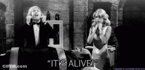 A Man In A Tuxedo Says " It 'S Alive " In Front Of A Woman In A White Dress GIF