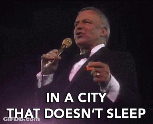 A Man In A Tuxedo Singing Into A Microphone With The Words In A City That Does N't Sleep GIF