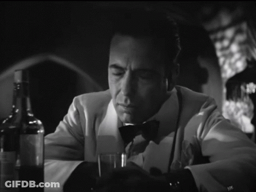 A Man In A Tuxedo Sits At A Table With A Glass Of Wine GIF