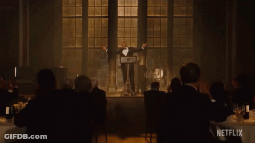 A Man In A Tuxedo Stands At A Podium In Front Of A Crowd With A Netflix Logo In The Corner GIF