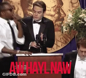 A Man In A Tuxedo Stands At A Podium With Aw Hayl Naw Written On It GIF