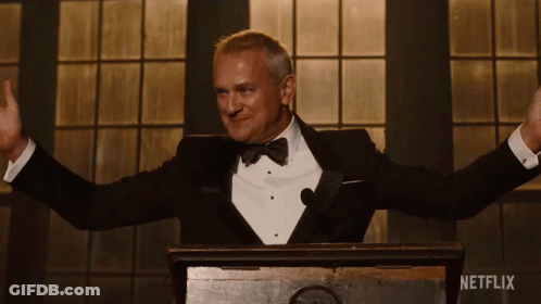 A Man In A Tuxedo Stands Behind A Podium With Netflix Written On The Bottom GIF