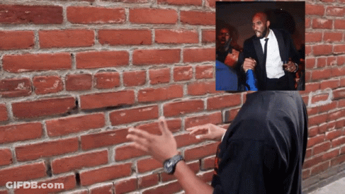 A Man In A Tuxedo Stands In Front Of A Brick Wall With His Hands Outstretched GIF