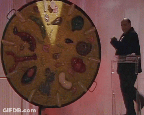 A Man In A Tuxedo Stands In Front Of A Large Circular Display Of Various Food Items GIF