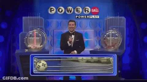 A Man In A Tuxedo Stands In Front Of A Powerball Lottery Machine GIF