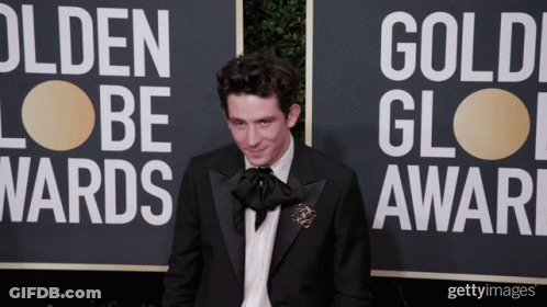 A Man In A Tuxedo Stands In Front Of A Sign That Says Golden Globes GIF