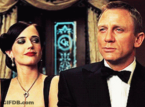 A Man In A Tuxedo Stands Next To A Woman In A Black Dress GIF