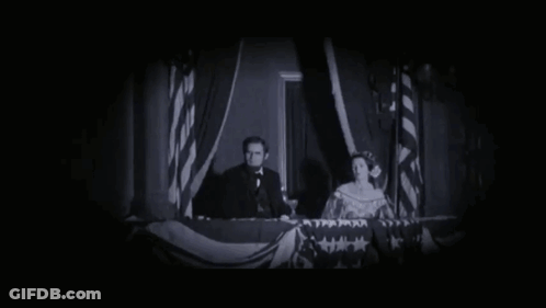 A Man In A Tuxedo Stands Next To A Woman In A Dress And A Man In A Suit GIF