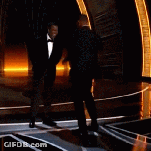 A Man In A Tuxedo Stands Next To Another Man In A Tuxedo On A Stage GIF