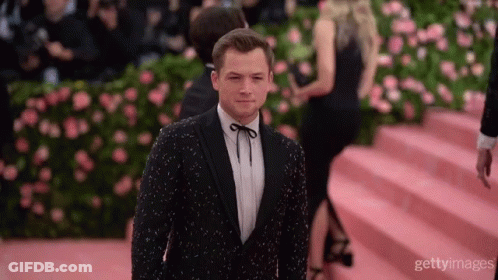 A Man In A Tuxedo Stands On A Red Carpet GIF