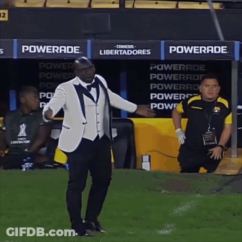 A Man In A Tuxedo Stands On A Soccer Field In Front Of A Powerade Advertisement GIF