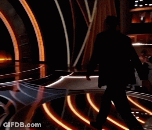 A Man In A Tuxedo Stands On A Stage With A Reflection Of Himself GIF