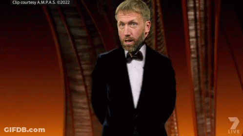 A Man In A Tuxedo Stands On A Stage With A Shield That Says Arsenal GIF